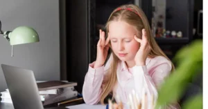 Young girl sitting at a desk holding her temples, appearing stressed while studying.